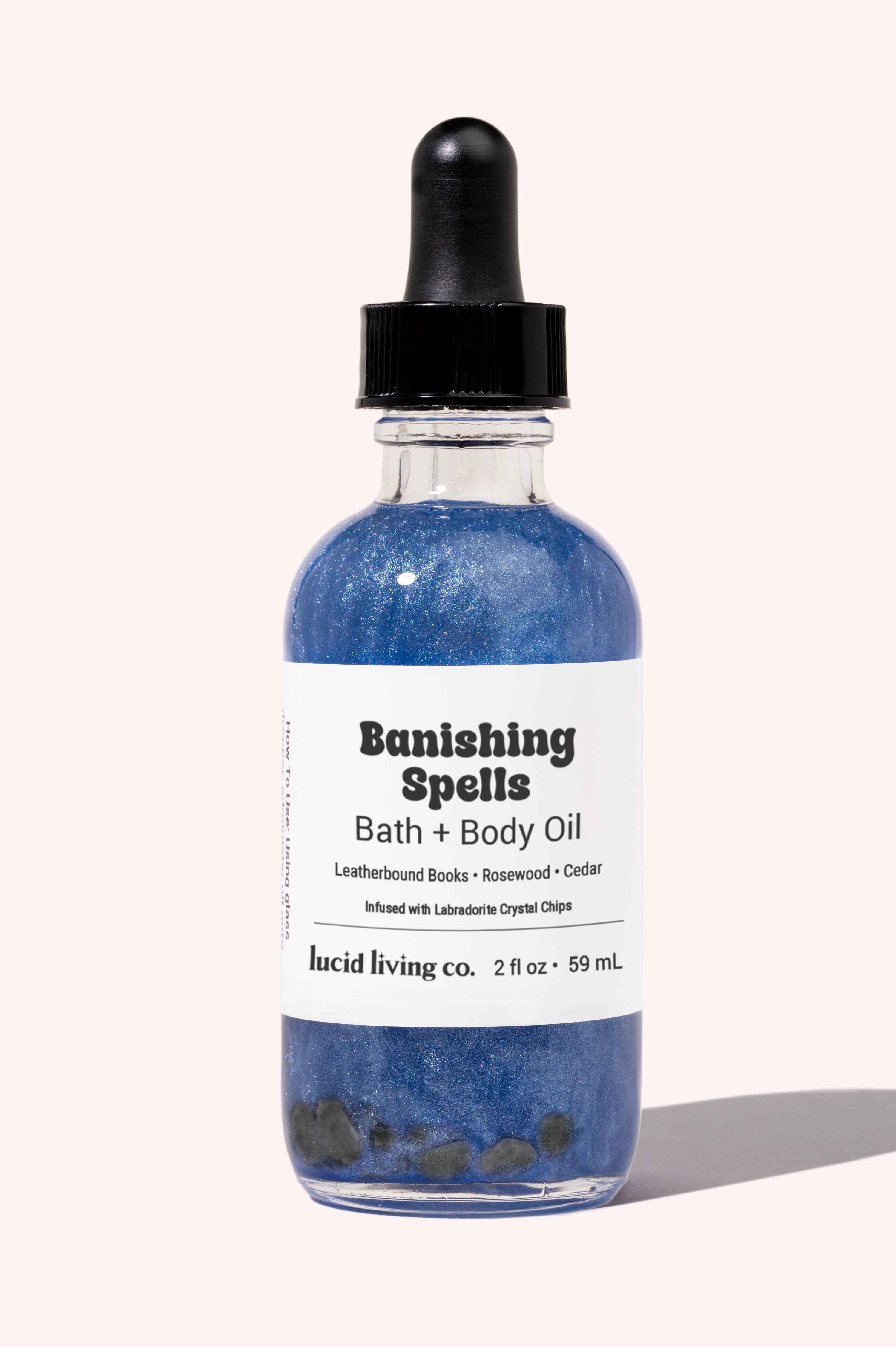Banishing Spells Bath & Body Oil bottle with shimmering blue liquid and labradorite crystal chips inside.