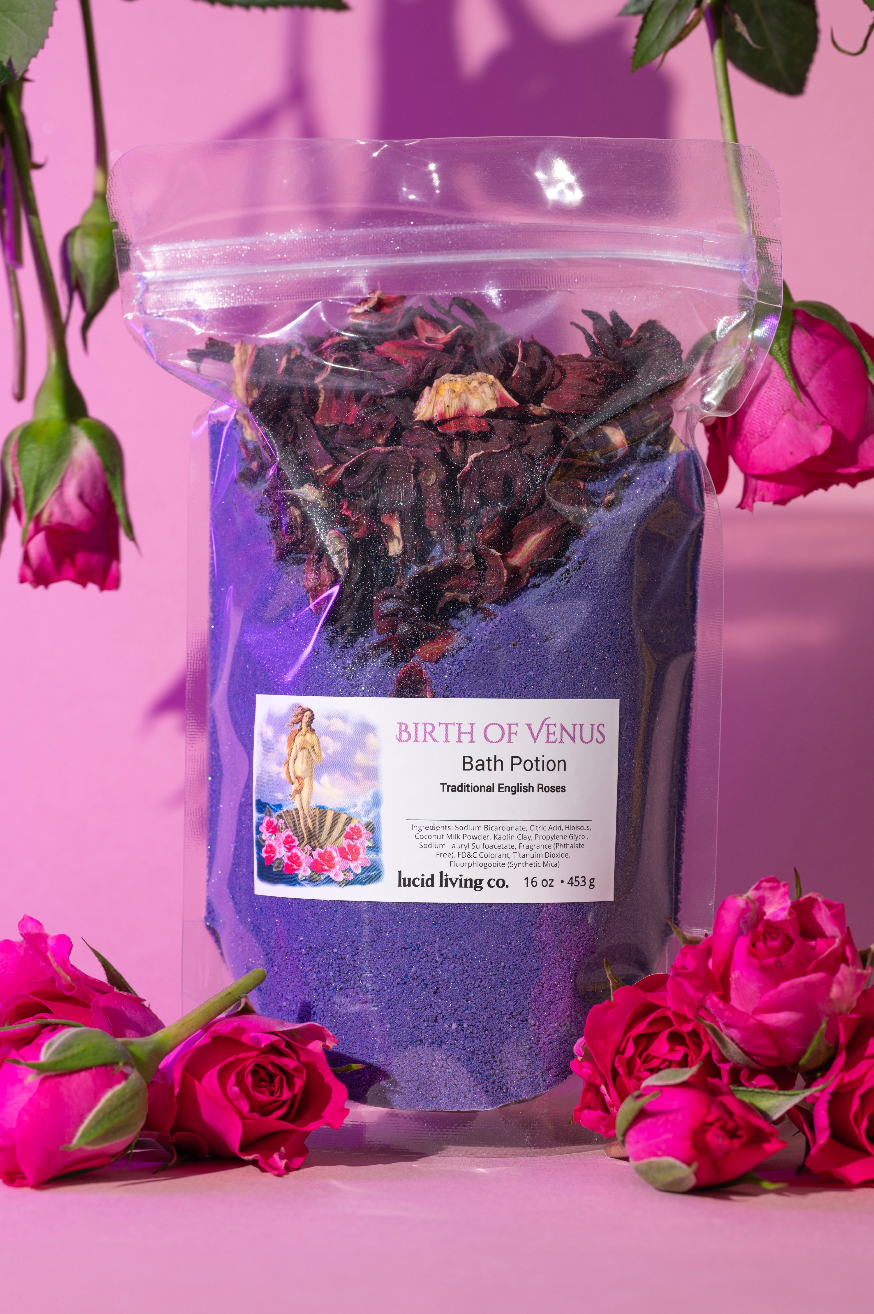 Birth of Venus Bath Potion with purple powder and dried flowers surrounded by pink roses on a pink background