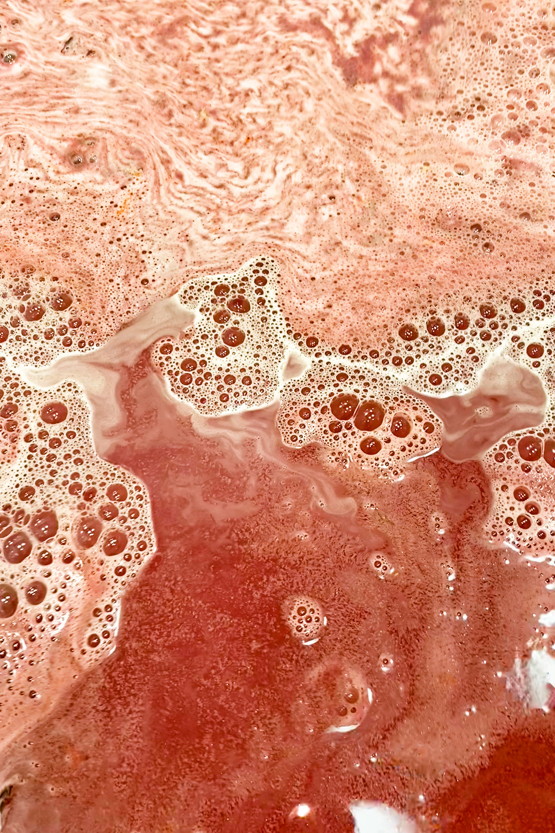 Close-up of swirling deep crimson bath water with foam from Daddy Dracula Bath Potion.