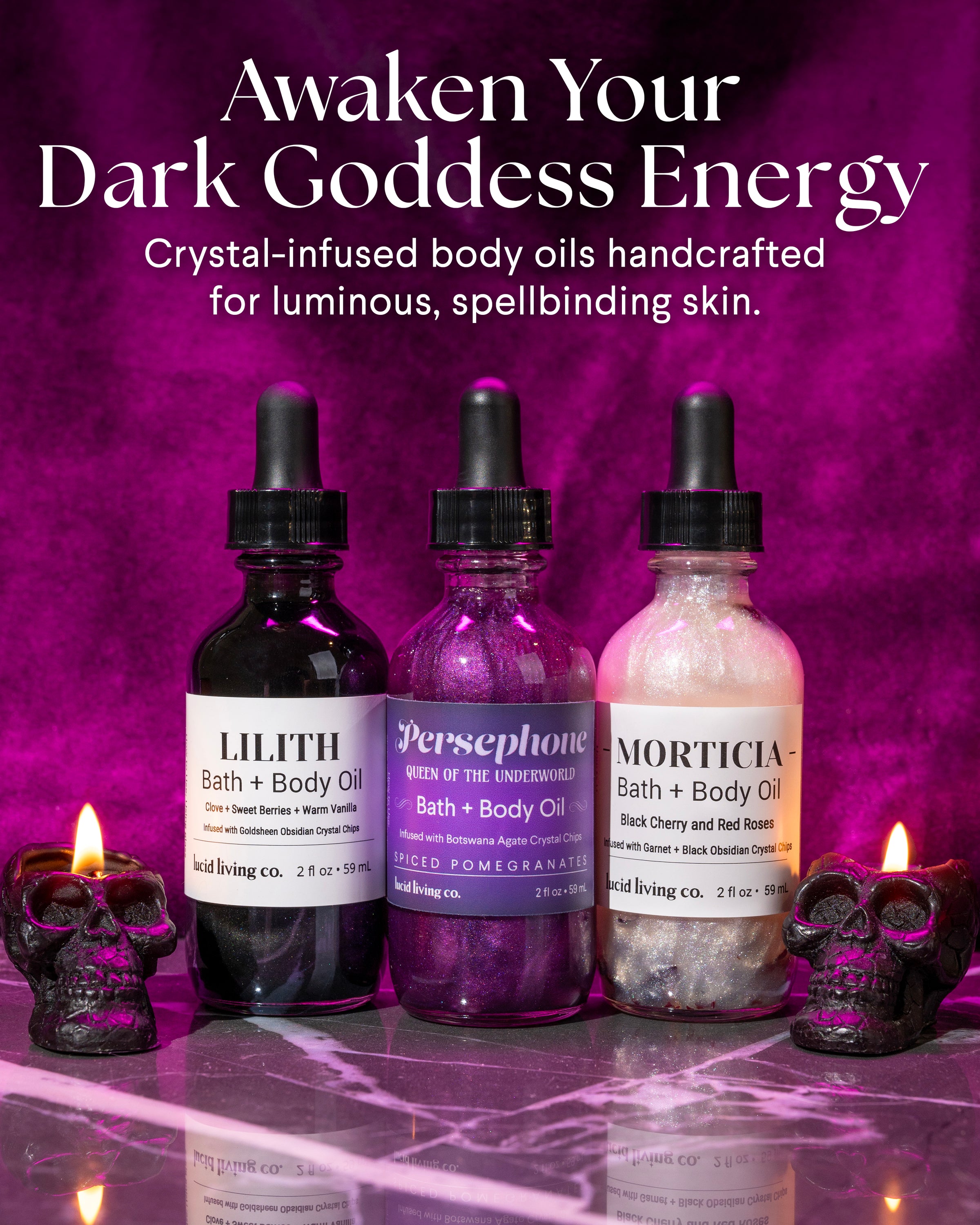 Three glass dropper bottles of crystal-infused bath and body oils in dark purple, magenta, and pearlescent white, displayed on a reflective purple surface with two glowing black skull candles nearby and a smoky purple backdrop.