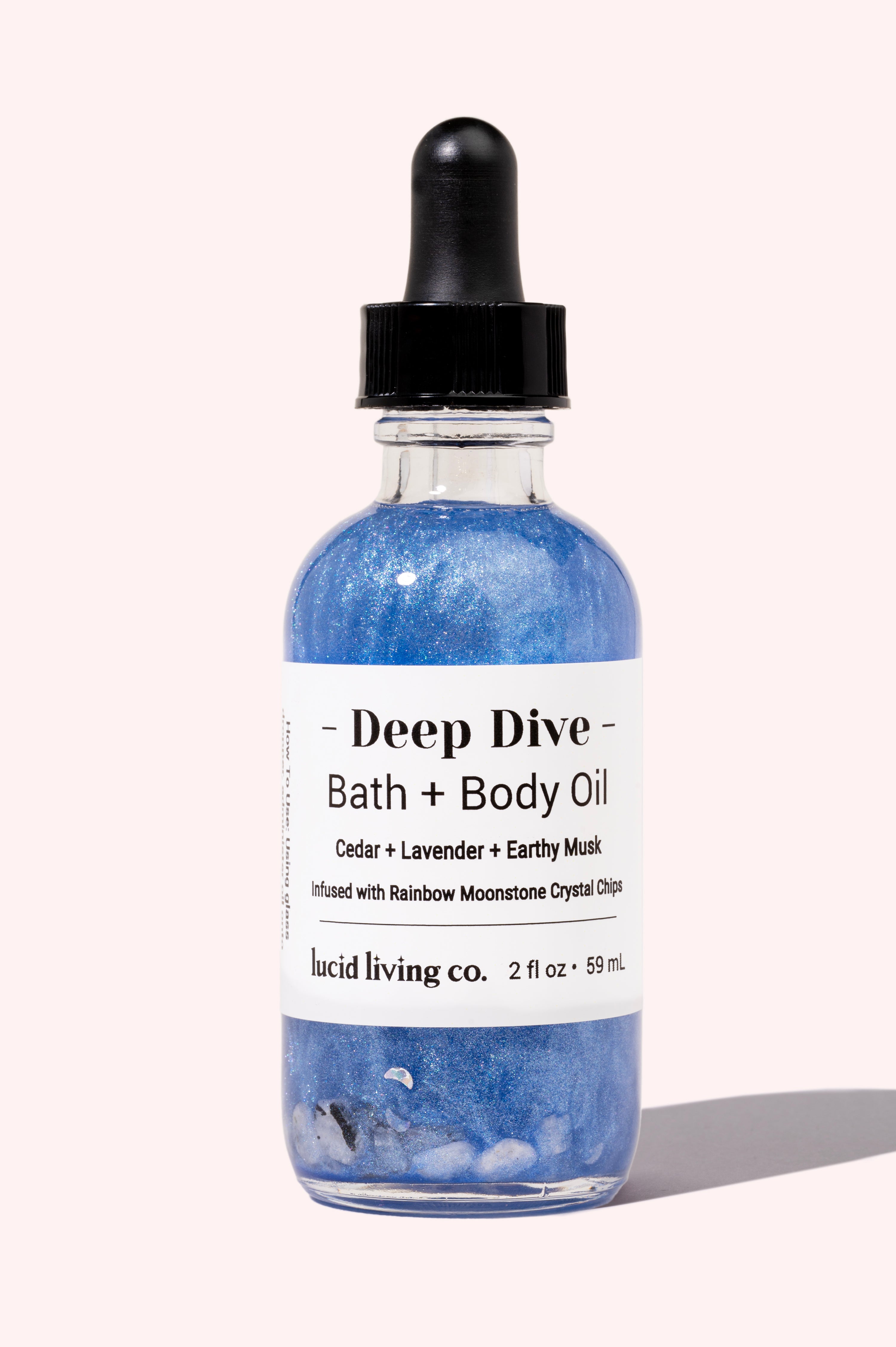 Deep Dive Bath & Body Oil with lavender, cedar, musk, and Rainbow Moonstone crystal chips in a blue shimmering bottle.
