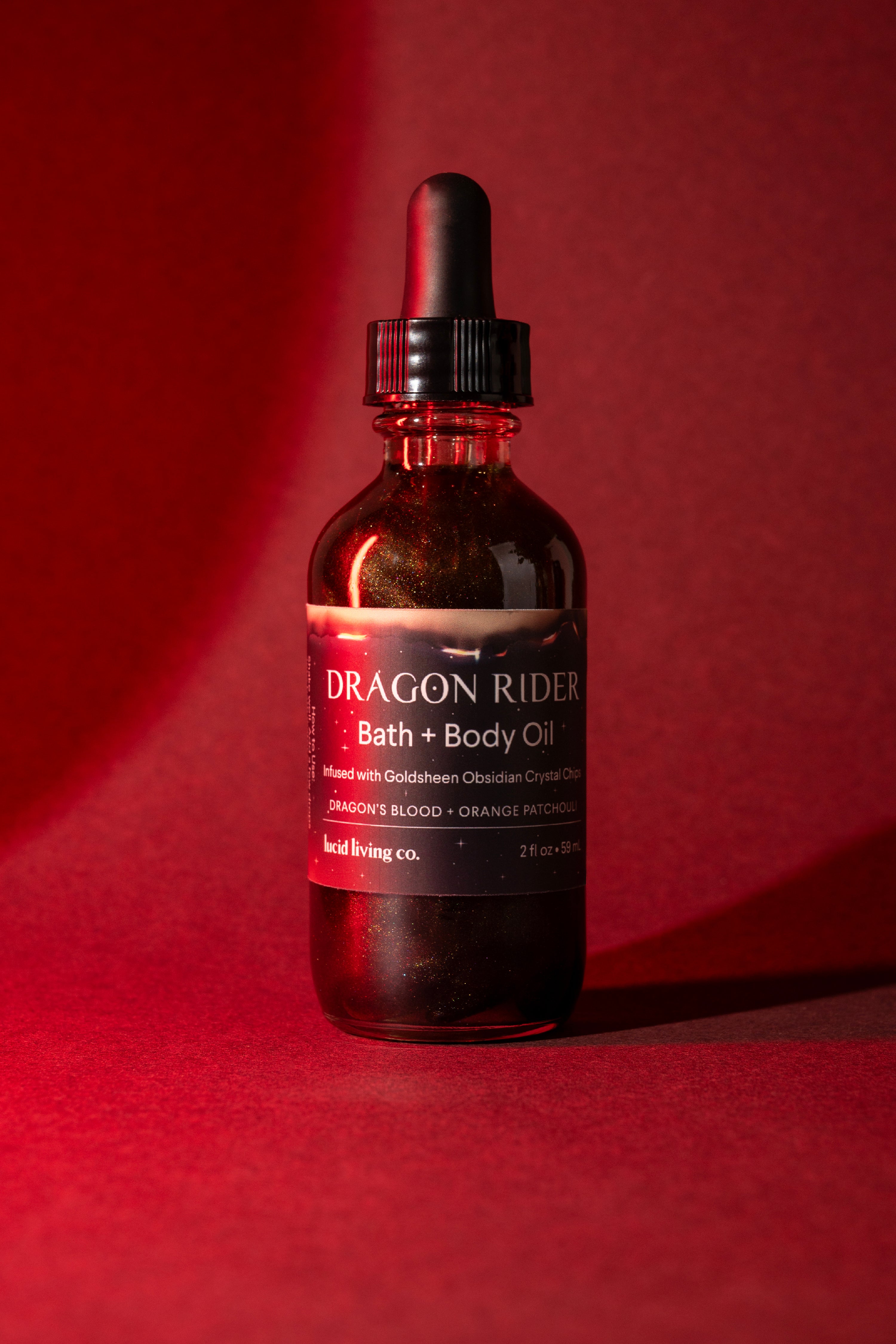 Dragon Rider Bath & Body Oil bottle with goldsheen obsidian chips against a red background.