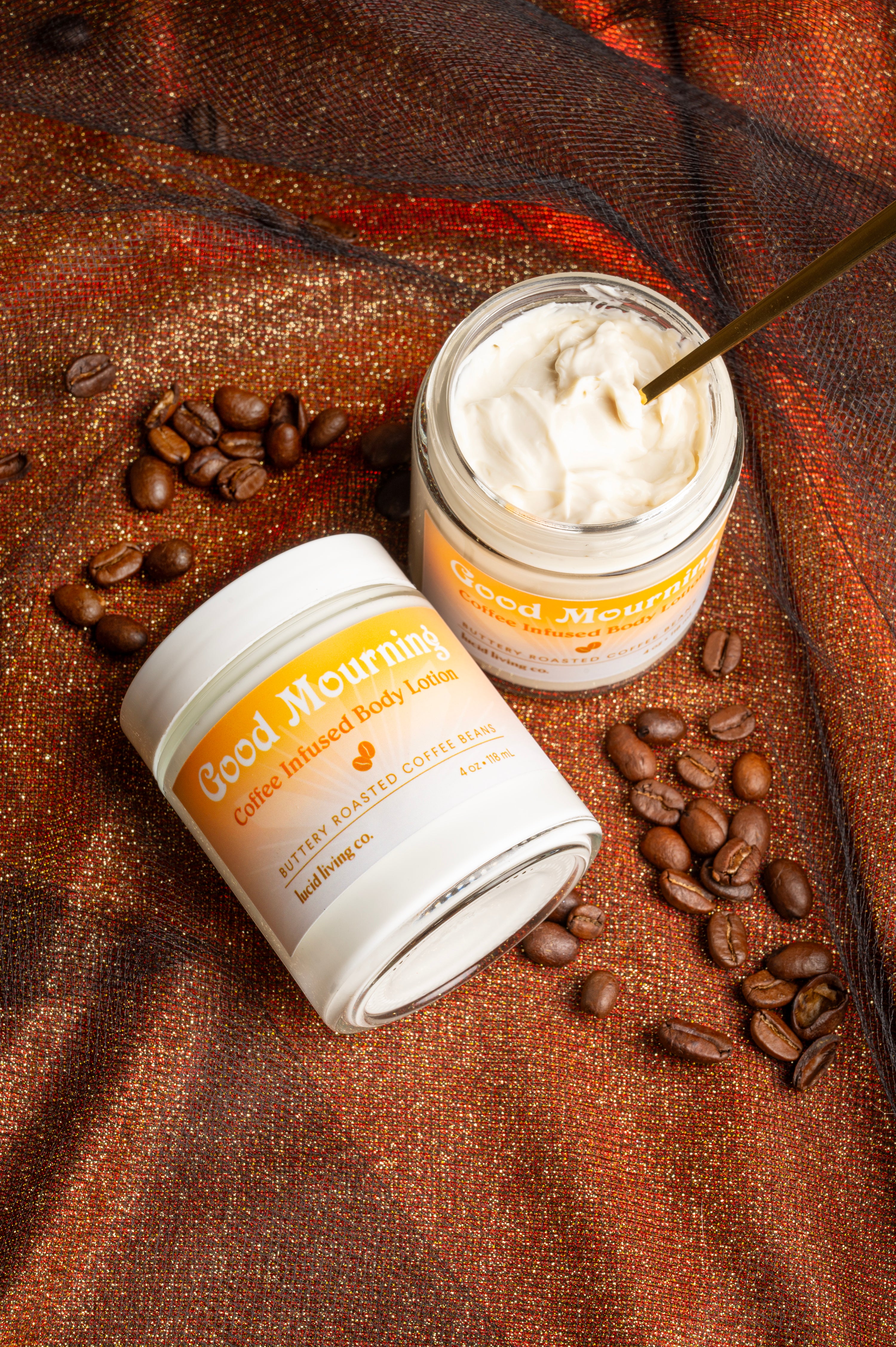 Good Mourning Coffee Infused Body Lotion with creamy texture and coffee beans on sparkling fabric background.