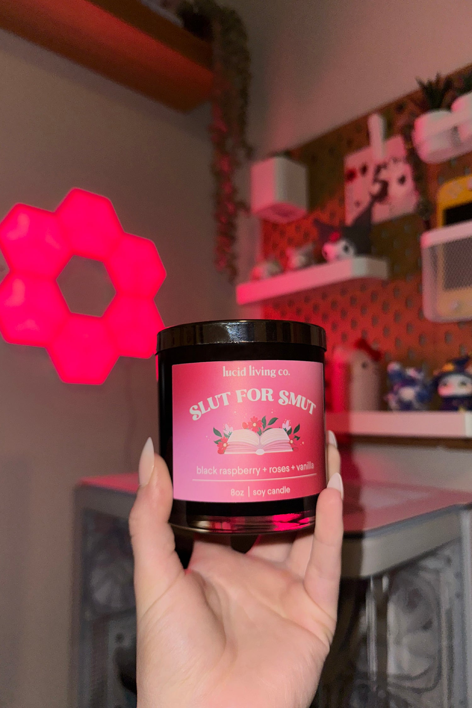 Hand holding Slut for Smut Soy Candle with black raspberry, roses, and vanilla scent label in cozy room setting