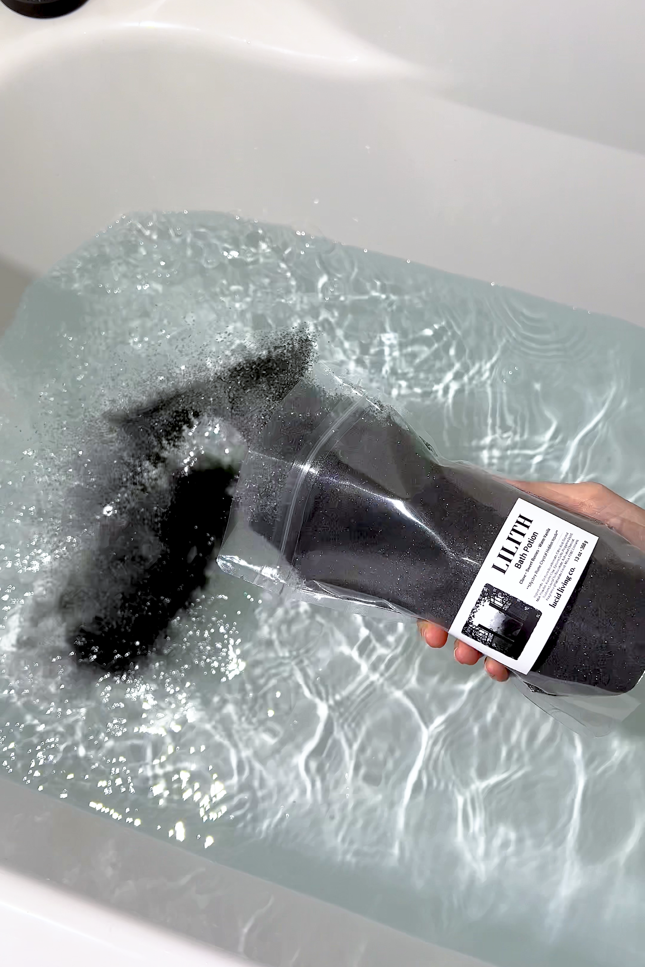 LILITH "The Dark Mother" Bath Potion being poured into a bathtub creating black bubbles and swirls in water.