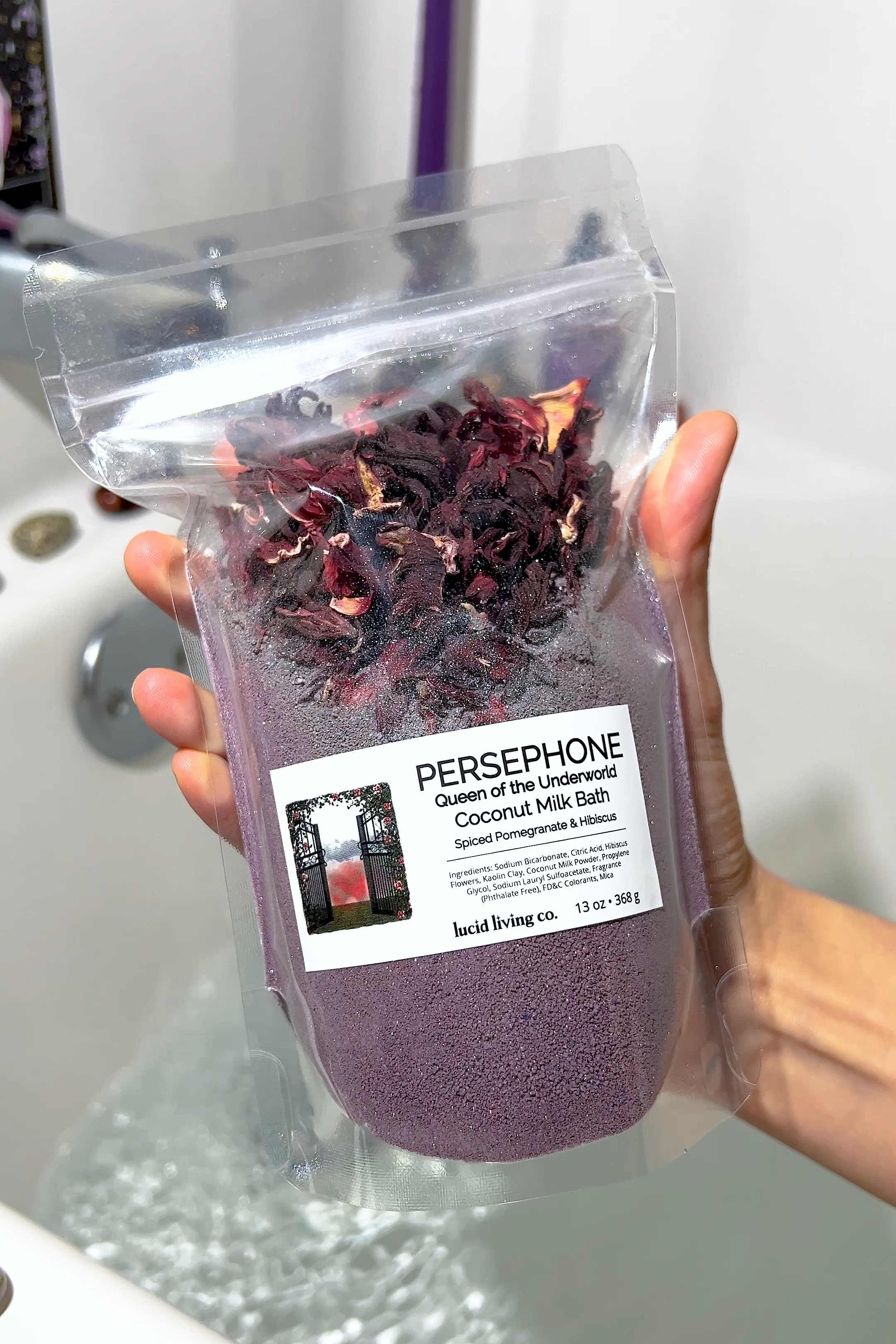 PERSEPHONE "Queen of the Underworld" Coconut Milk Bath with spiced pomegranate and hibiscus in clear pouch held over bathtub.