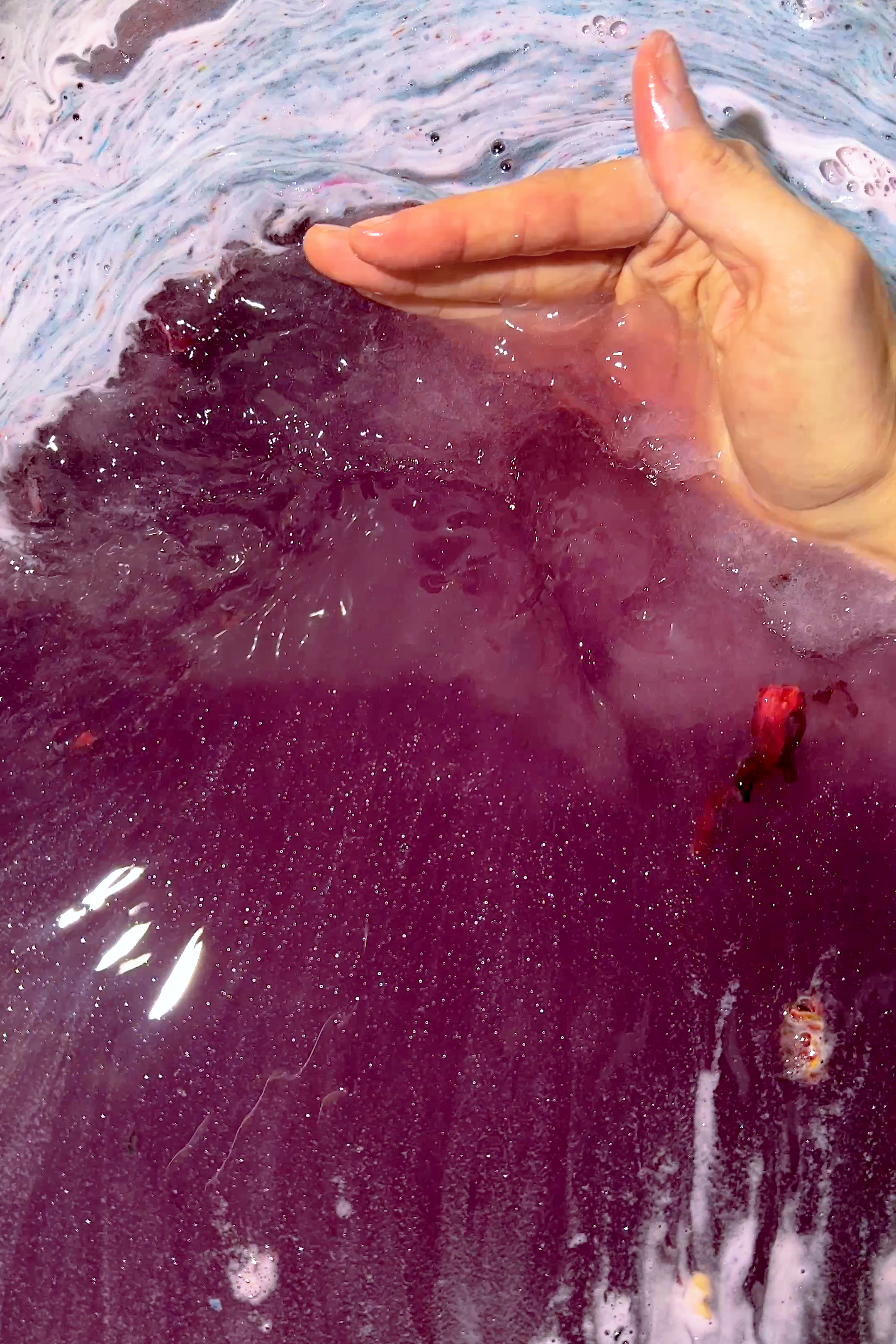 Hand stirring vibrant purple water with bubbles from PERSEPHONE "Queen of the Underworld" Coconut Milk Bath product.