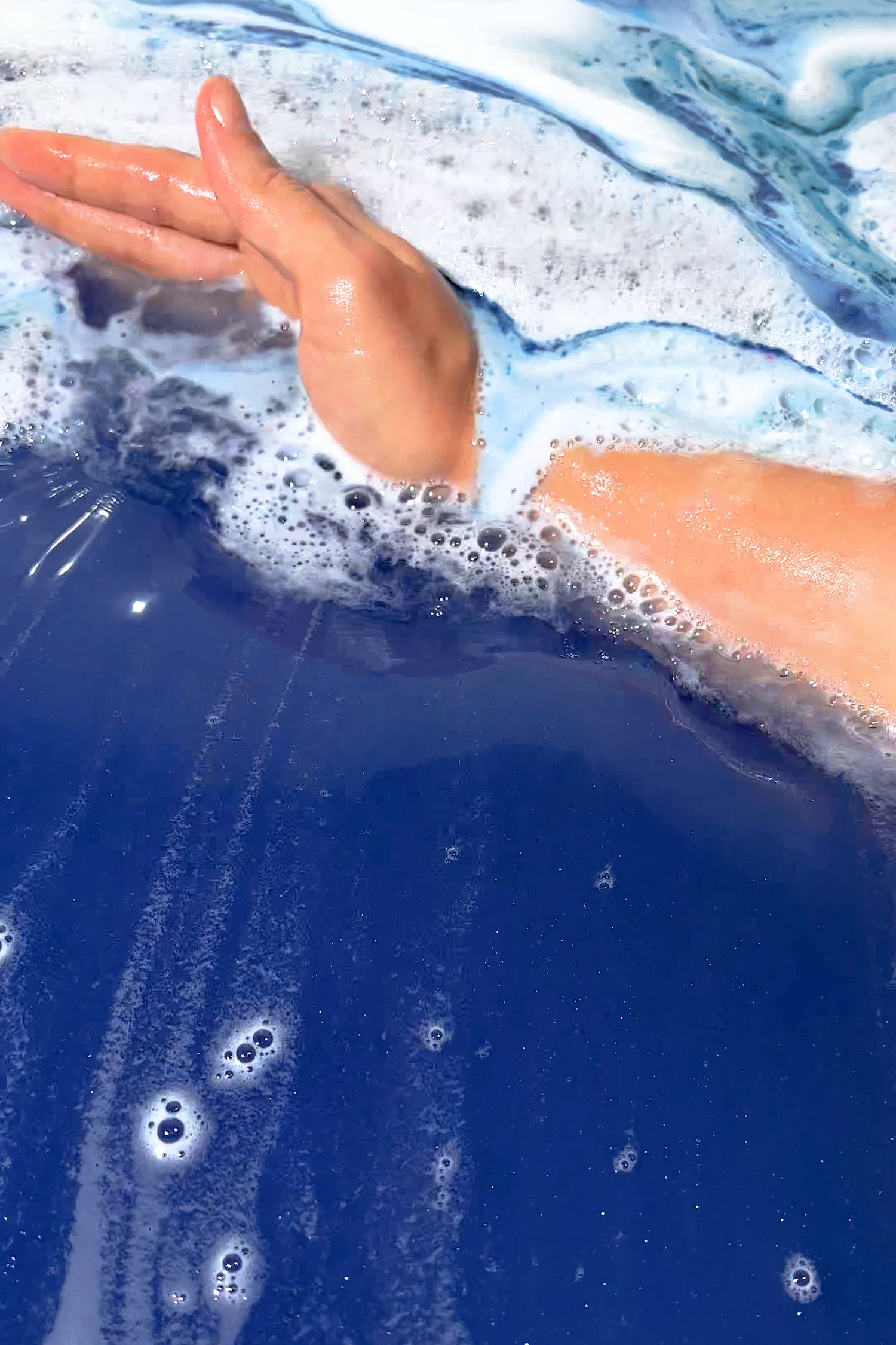 Hand immersed in dark blue bubbly water showcasing Just the Tip, I Promise Bath Potion relaxing bath experience.