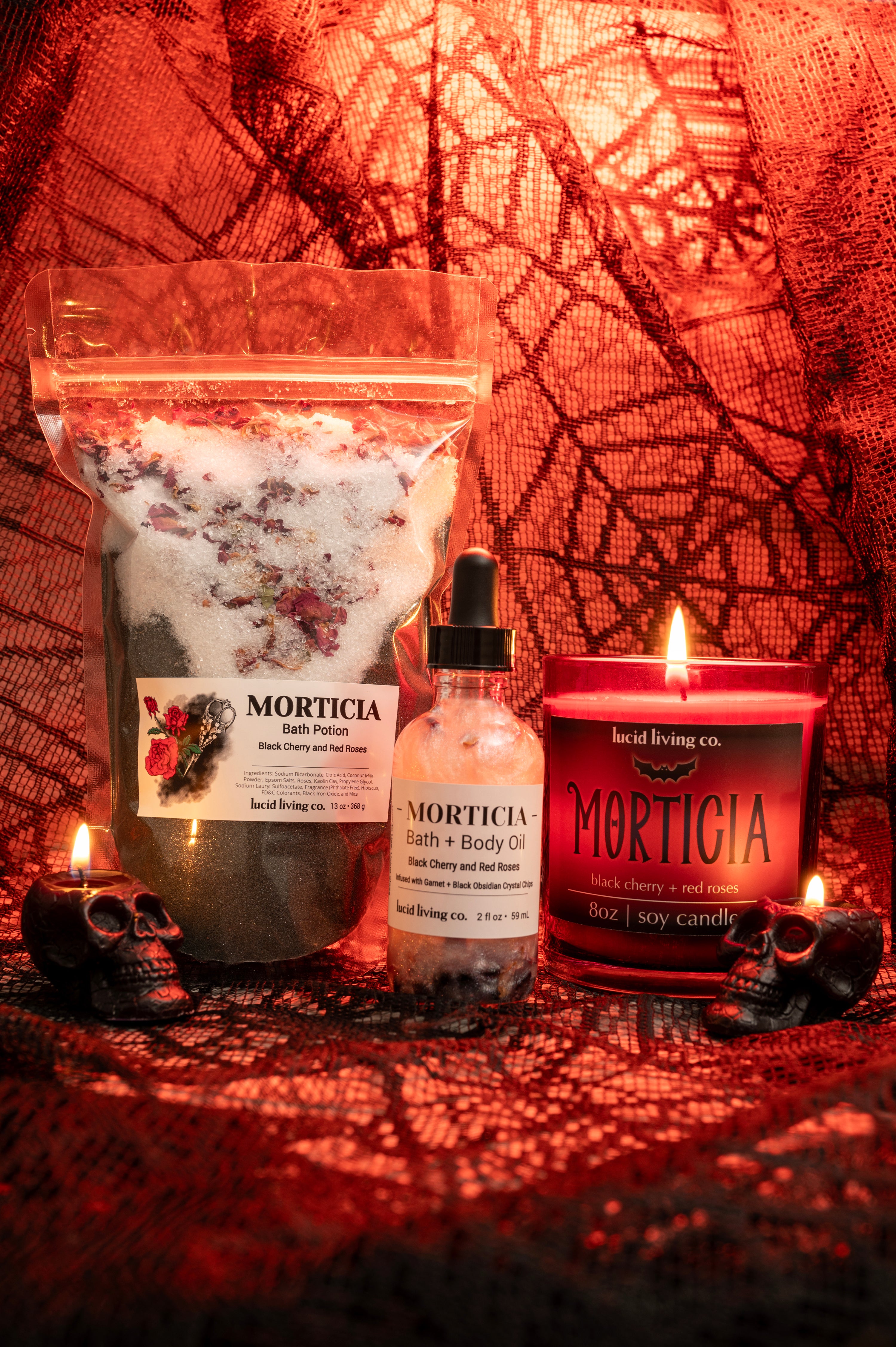 MORTICIA Bundle with black cherry bath potion, body oil, and soy candle on red spiderweb background with skull candles.