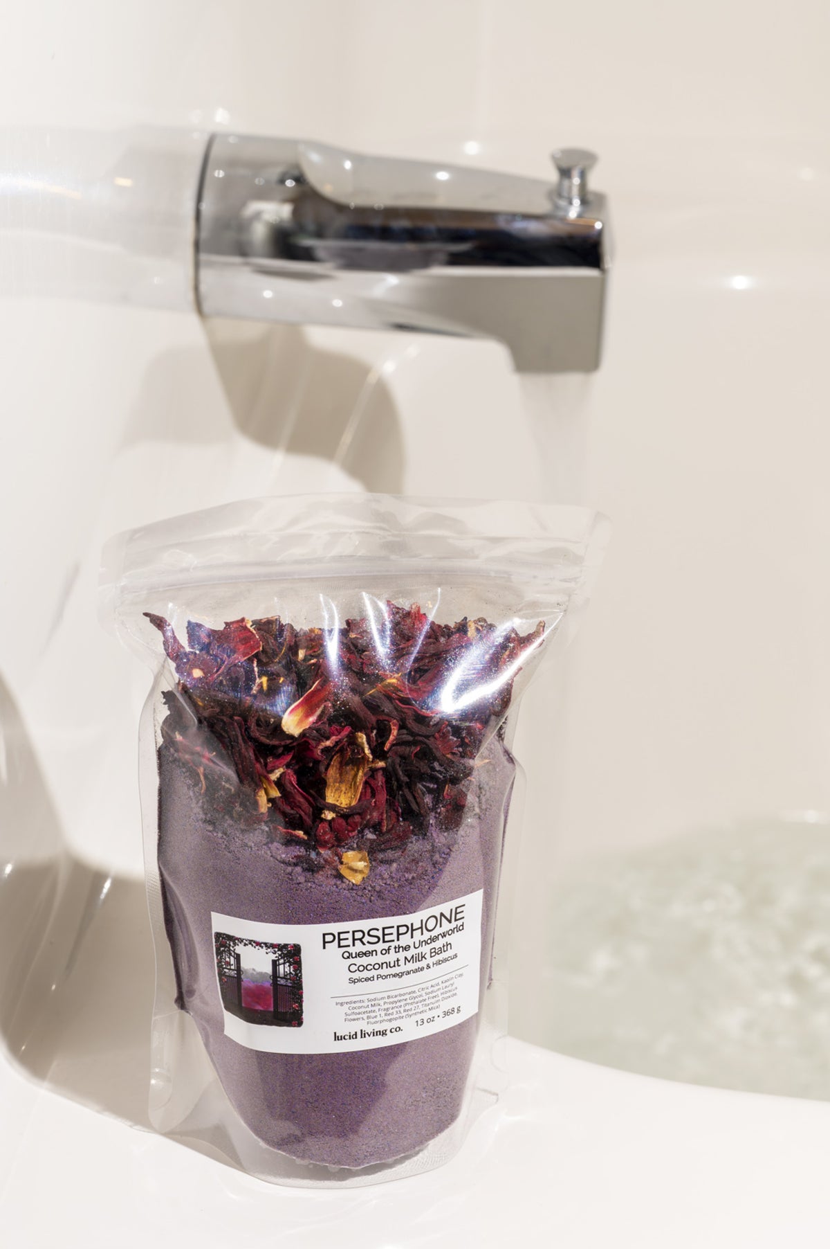 PERSEPHONE "Queen of the Underworld" Coconut Milk Bath with spiced pomegranate and hibiscus flowers in clear bag near faucet