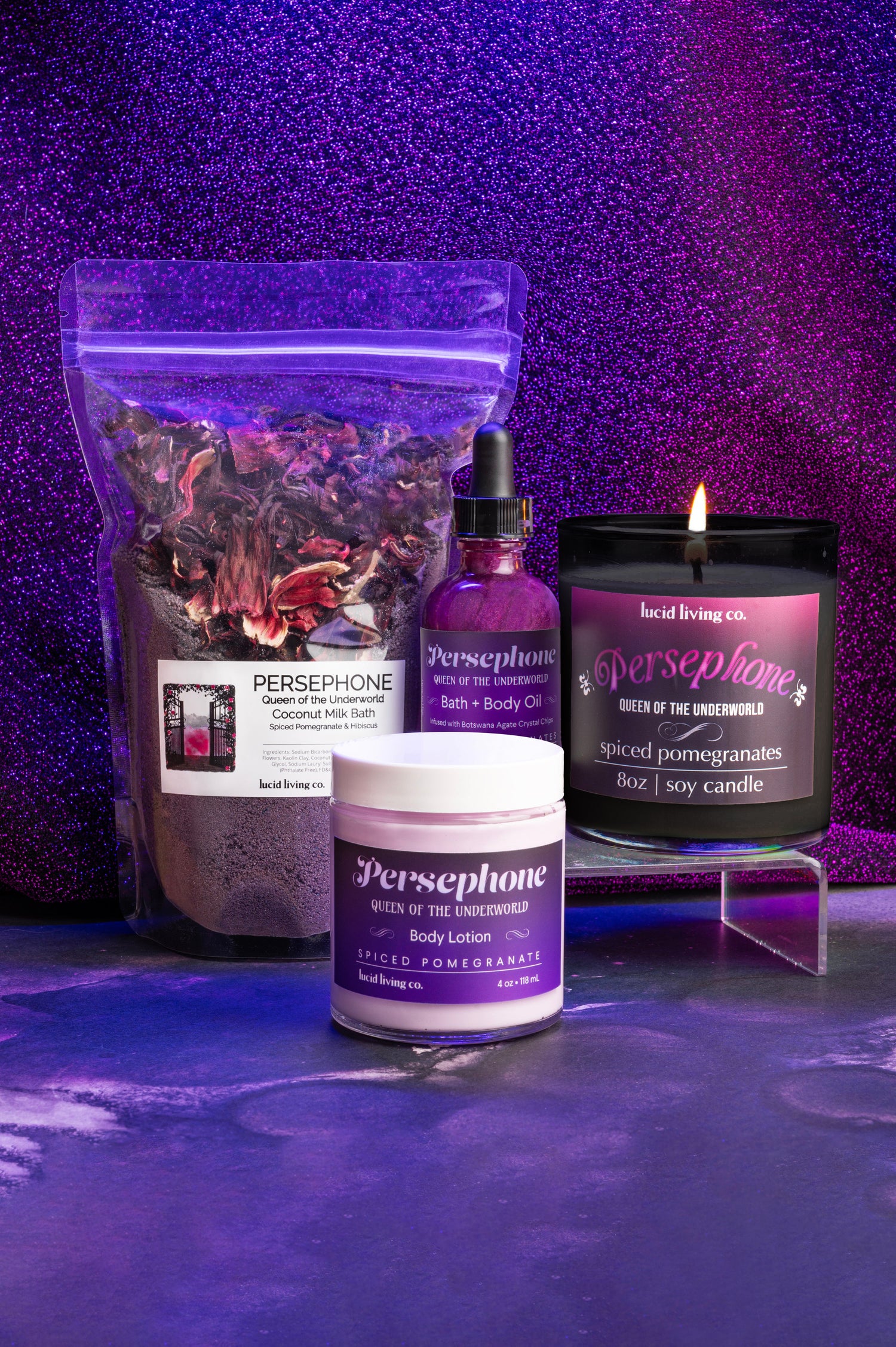Persephone Bundle with spiced pomegranate bath milk, bath oil, body lotion, and soy candle on purple glitter background