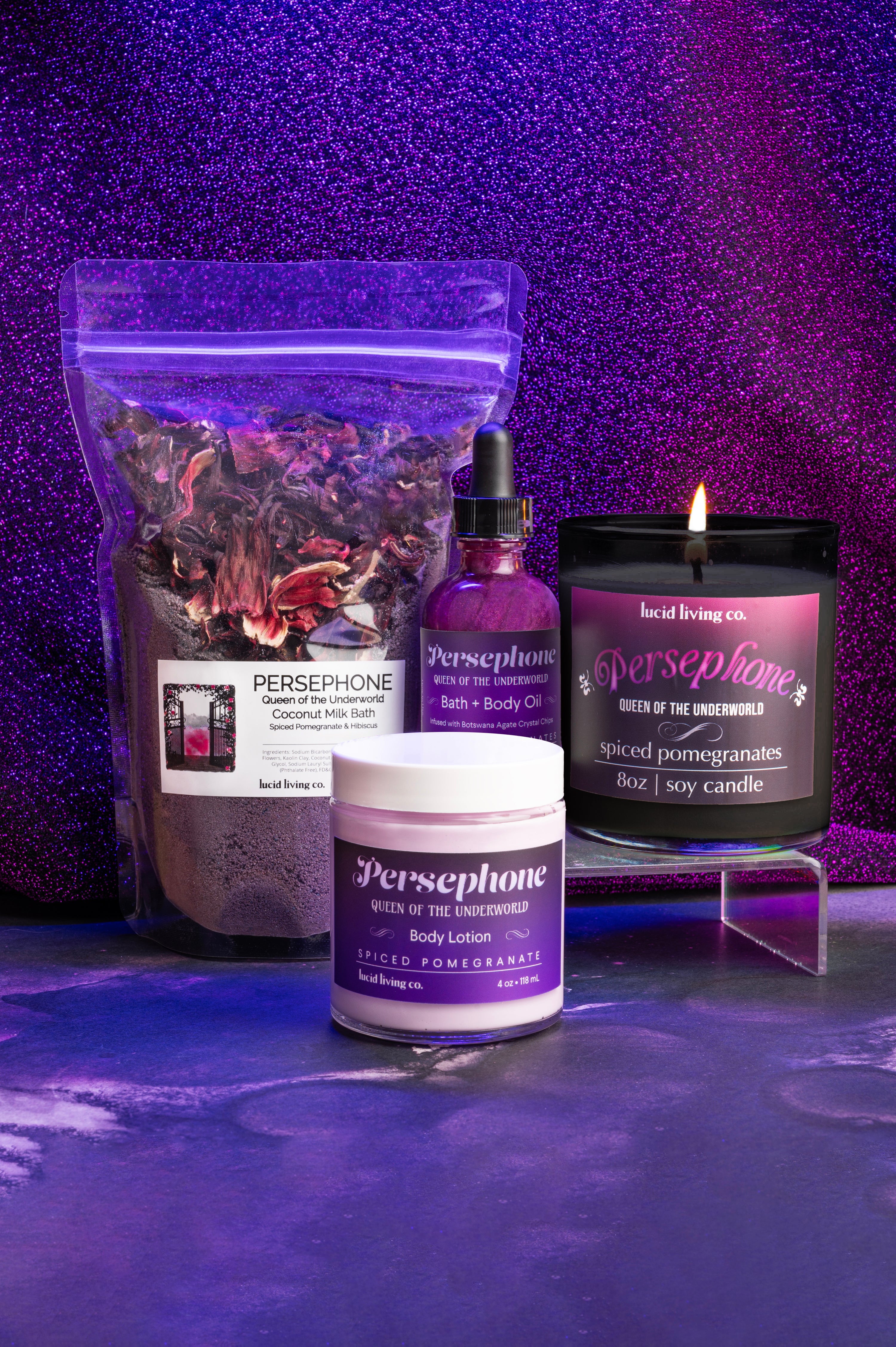 Persephone Bundle with spiced pomegranate bath milk, bath oil, body lotion, and soy candle on purple glitter background