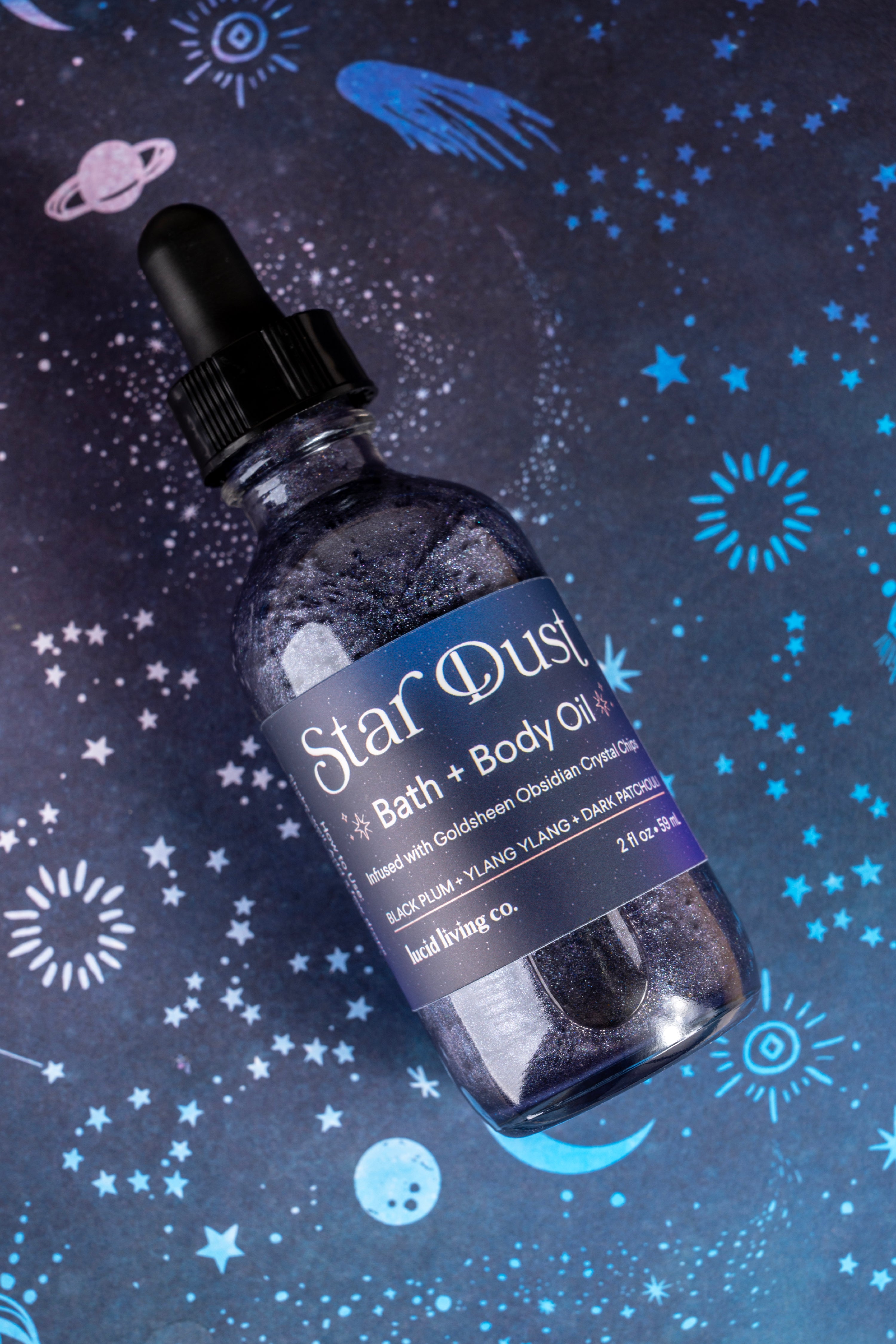 Star Dust Bath & Body Oil bottle with glittery liquid and celestial background featuring stars and planets.