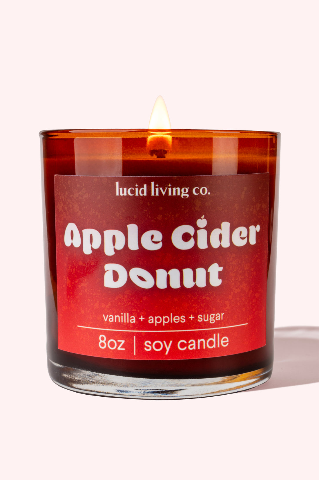 Apple Cider Donut Soy Candle burning in amber glass jar with vanilla, apple, and sugar scent label.