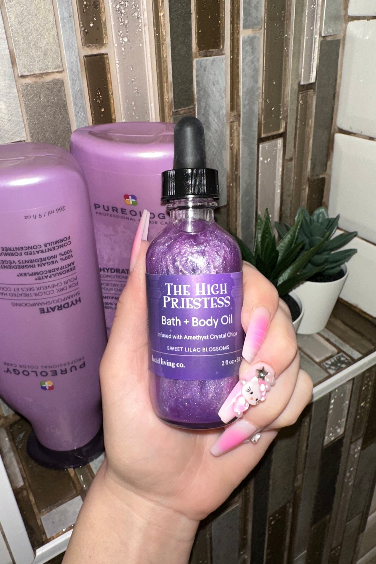 The High Priestess Bath &amp; Body Oil with amethyst crystal chips and sweet lilac blossoms in a purple bottle.