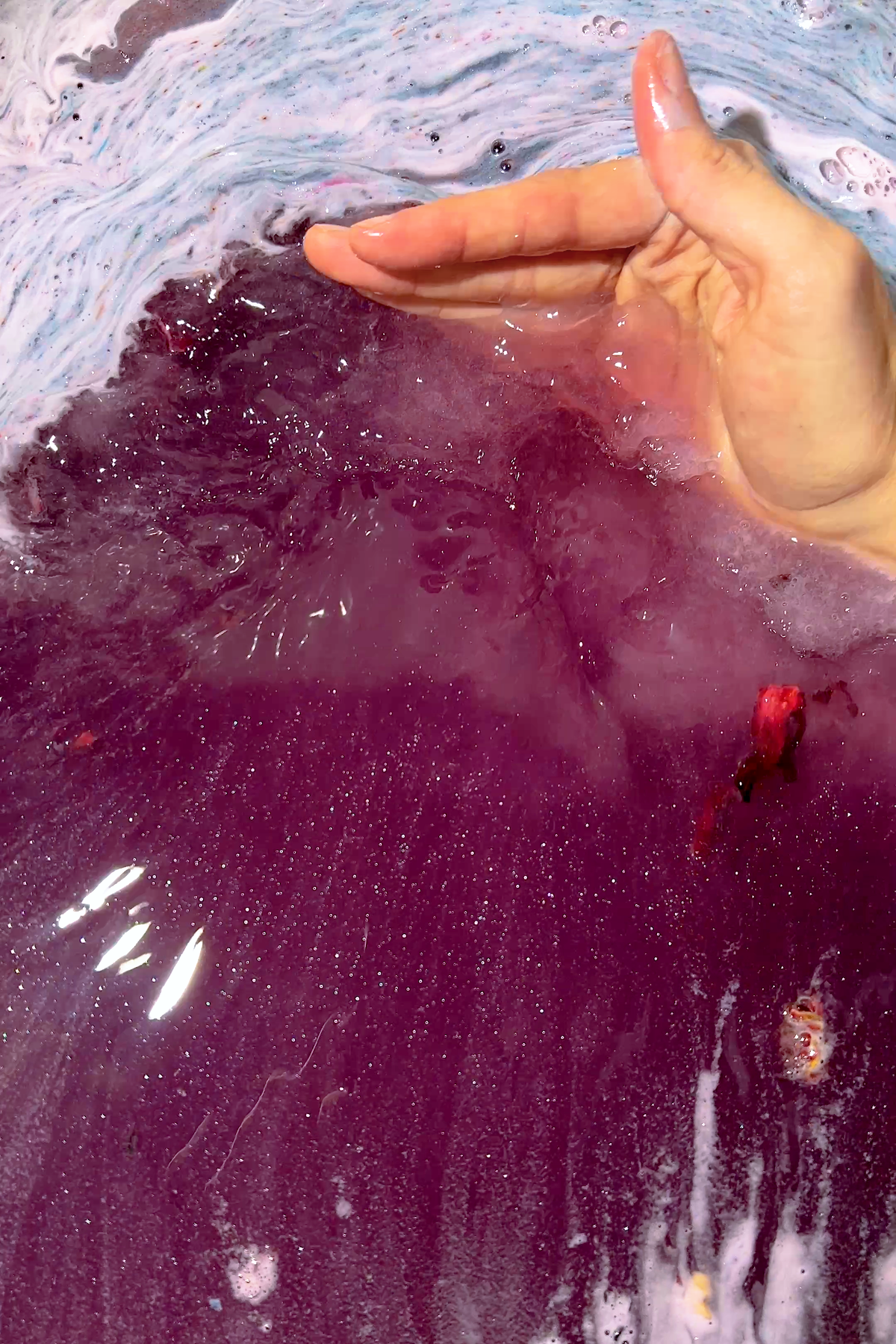 Hand stirring vibrant purple water with bubbles from PERSEPHONE "Queen of the Underworld" Coconut Milk Bath product.