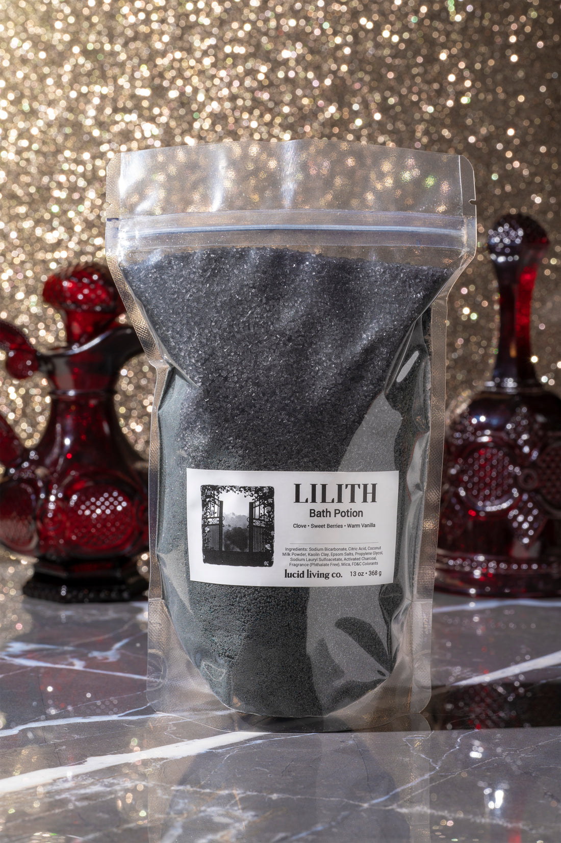 LILITH "The Dark Mother" Bath Potion in black granules with vintage red glass decor and glittery gold background.