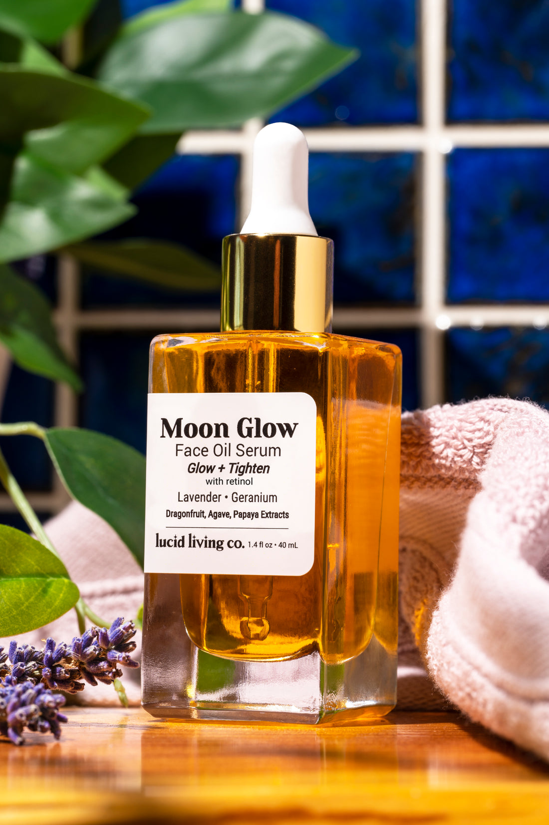 Moon Glow Face Oil Serum bottle with dropper, surrounded by lavender and soft fabric on wooden surface.