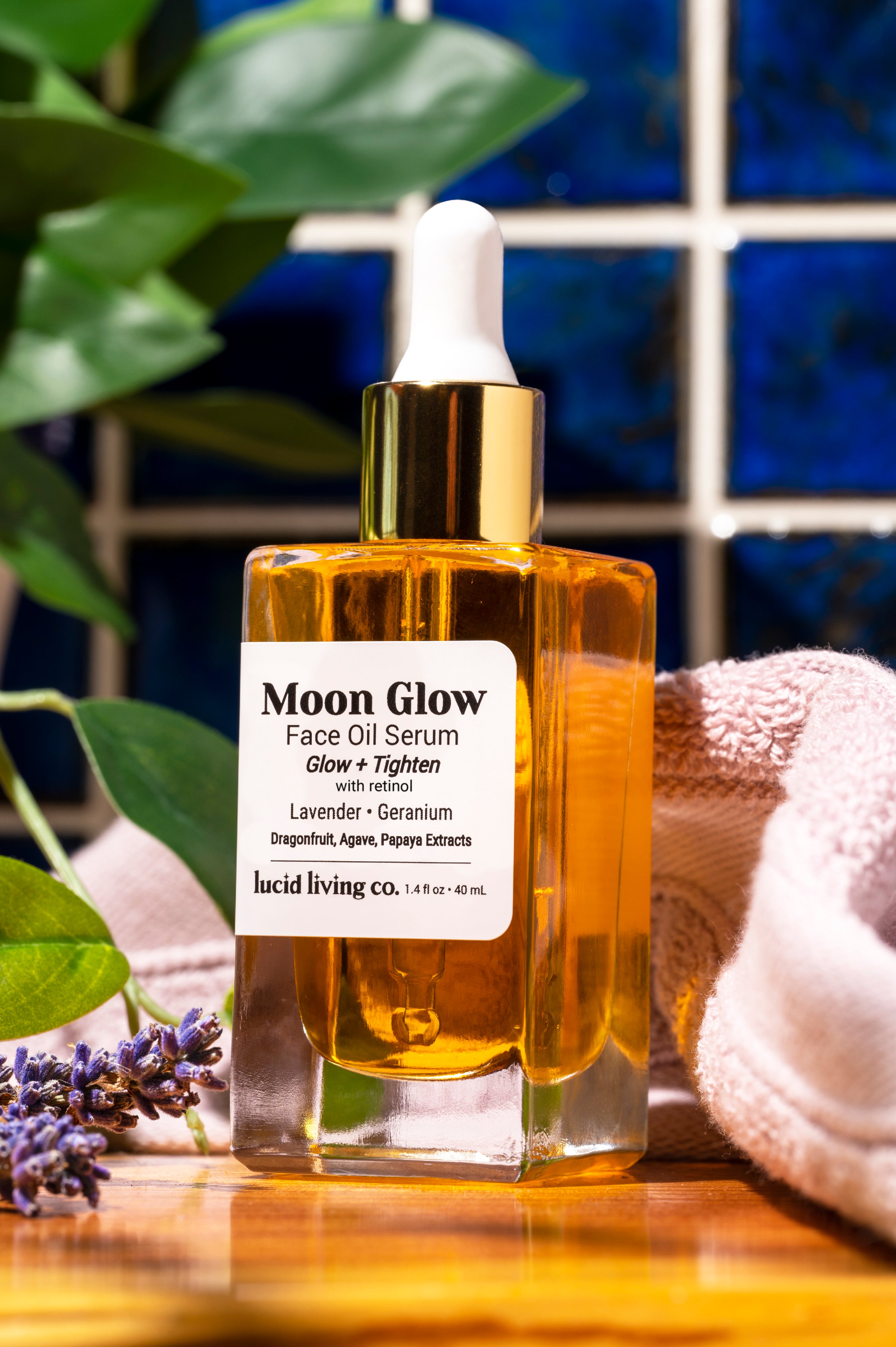 Moon Glow Face Oil Serum bottle with dropper, surrounded by lavender and soft fabric on wooden surface.