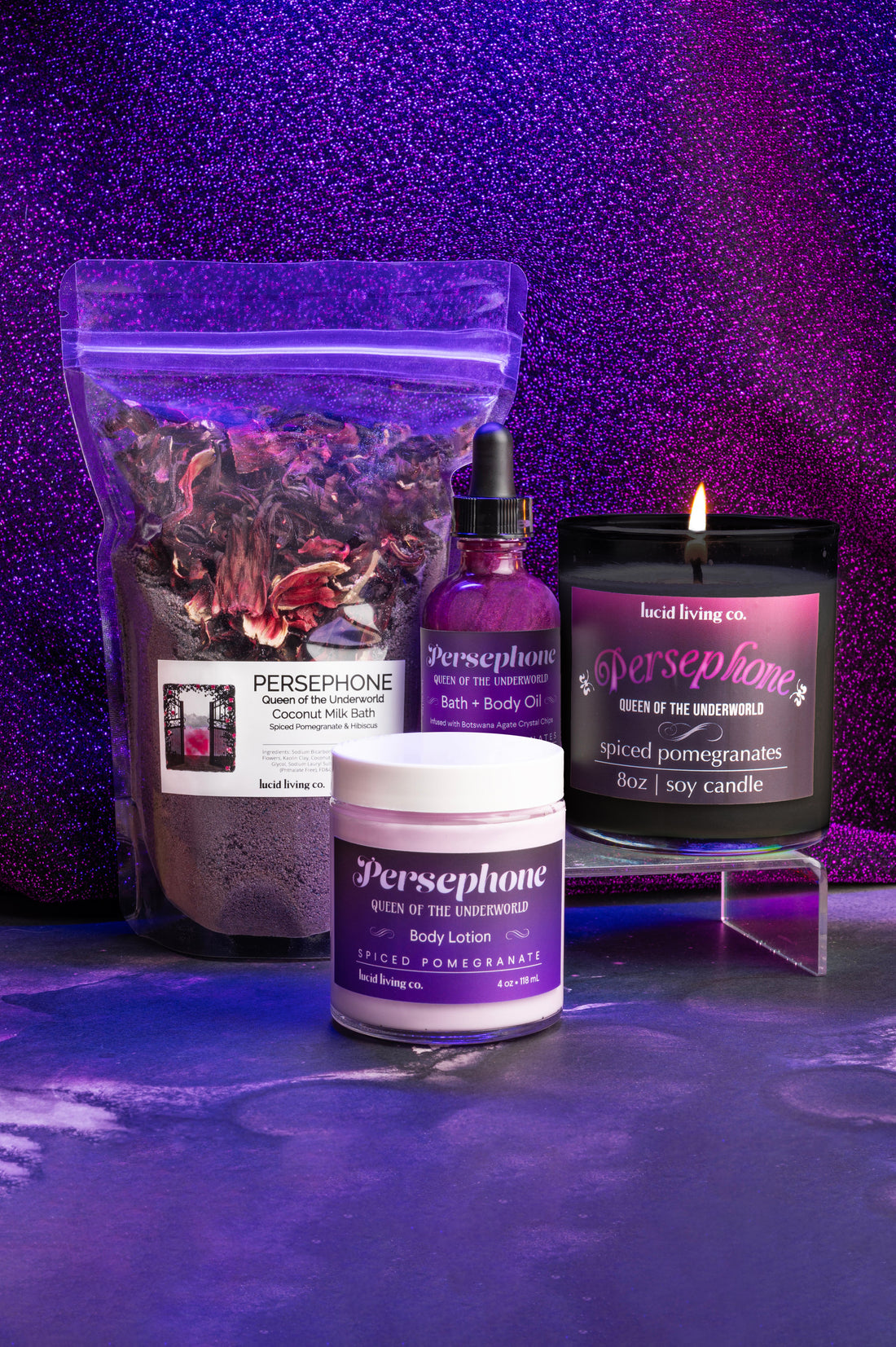 Persephone Bundle with spiced pomegranate bath milk, bath oil, body lotion, and soy candle on purple glitter background
