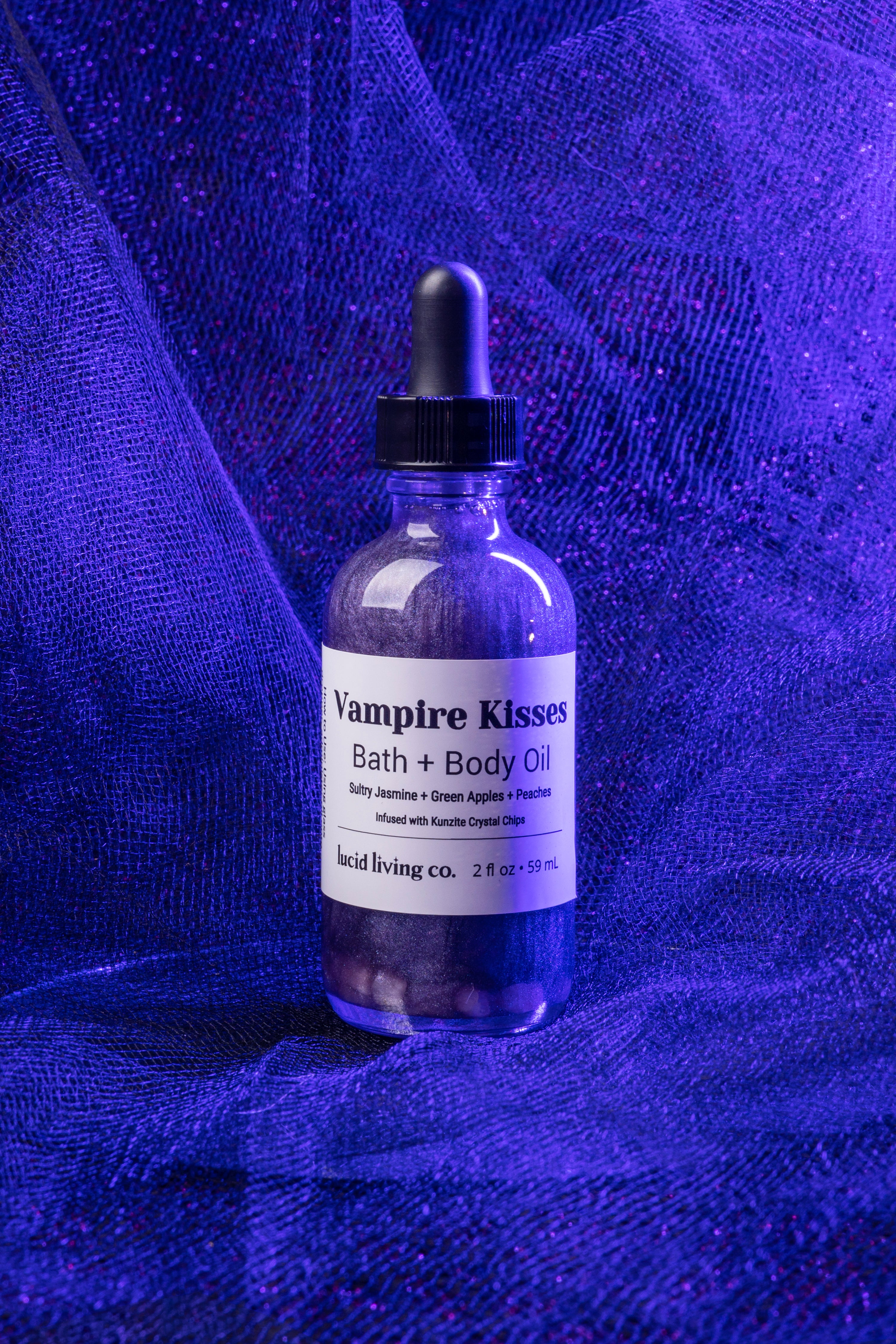 Vampire Kisses Bath &amp; Body Oil bottle with Kunzite crystal chips on purple textured fabric background