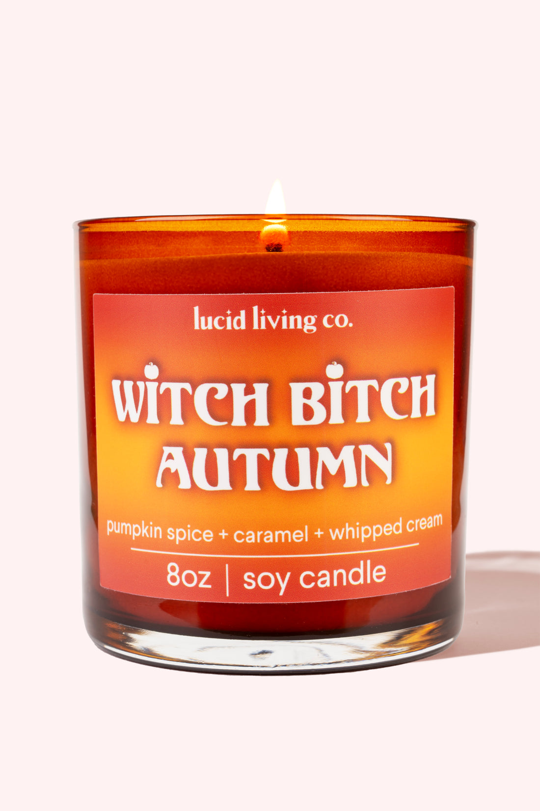 Witch Bitch Autumn Soy Candle burning with pumpkin spice caramel and whipped cream scent in amber glass jar.