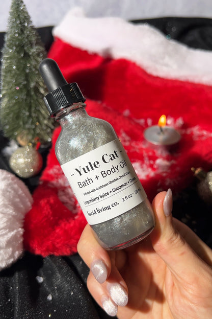 Bottle of Yule Cat Bath + Body Oil held by a hand with a festive background.